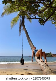 Female dressed blue swim suite lying and relaxing on the coconut palm tree trunk with hanging swing wheel and suntanning on the sandy Indian ocean beach, Mirissa district^ Sri Lanka.