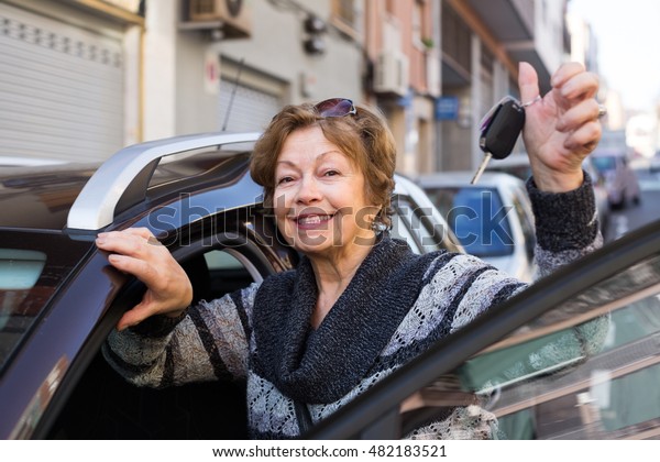Female driver 60-75 years old  standing with car\
key outdoor