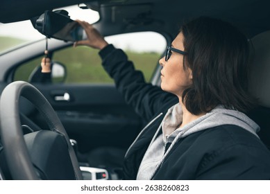 Female Driver In A Car Adjusts The Rearview Mirror