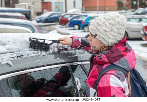 Female driver is cleaning snow with brush from the\
car roof