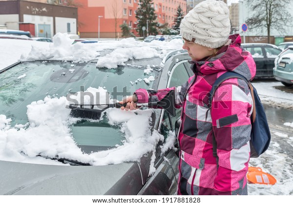 Female driver is cleaning snow with brush from\
the car windshield