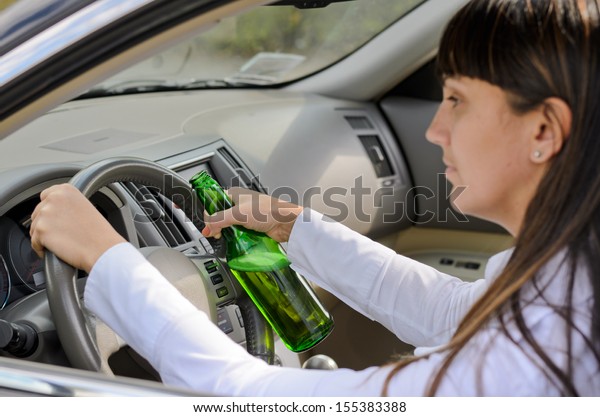 Female driver drinking and driving\
while grinning out of the side window as she clutches the steering\
wheel with her bottle of alcohol clasped in one\
hand