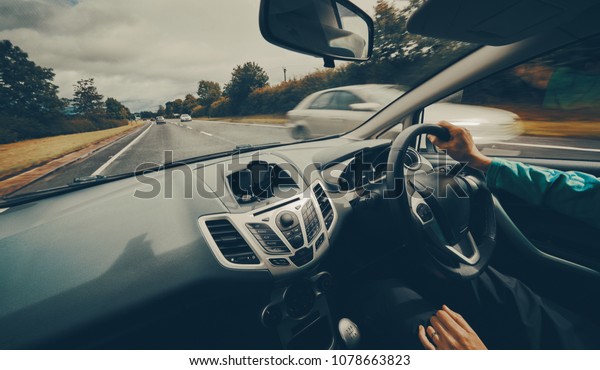 A female driver driving a car along a busy road\
on an English single carriageway on a cloudy overcaste day. Filter\
and colour styling applied.