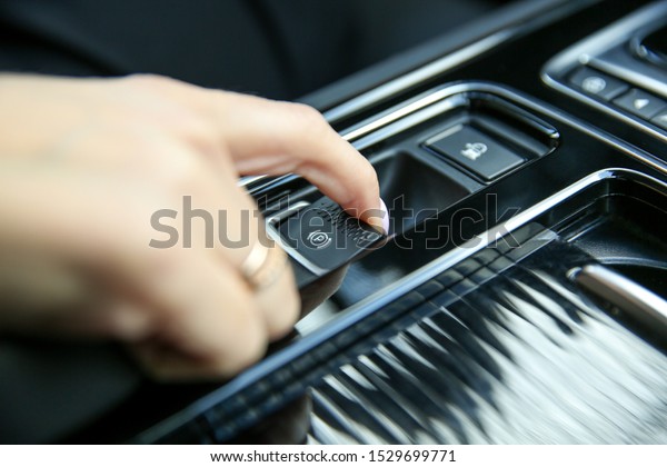 female driver finger pulls electronic parking\
brake button