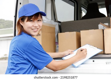 A female driver of light cargo is filling out paperwork. She is wearing a blue polo shirt and cap.