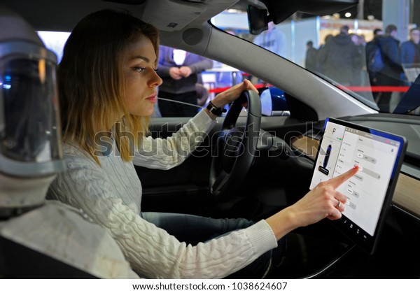 Female driver manipulating a touch\
screen monitor in cabin of an electric car. Exhibition PLUG-IN\
UKRAINE 2018. March 2, 2018. Kiev Expo center. Kiev,\
Ukraine