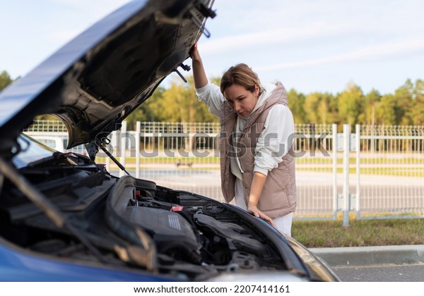 female\
driver next to the open hood of a broken down\
car