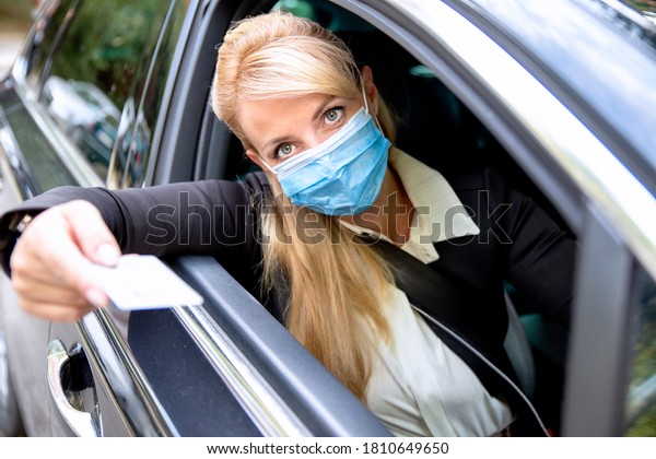 Female driver with protective face\
mask paying from the car or giving ID on the border. Woman with\
Driver\'s licence in hand for traffic violation on the\
road.