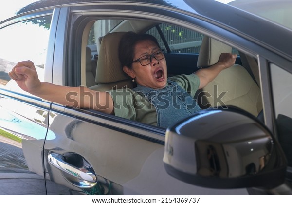 Female driver sitting in\
her car behind steering wheel, yawning and looking very tired and\
sleepy