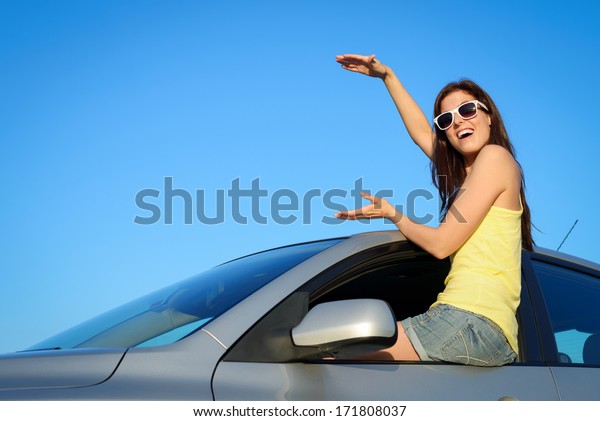 Female driver sitting on new car window\
holding virtual copy space for banner. Young woman on summer\
roadtrip. Driving license or vehicle rental\
concept.
