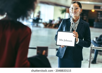 Female Driver Wearing Face Shield Standing At Airport Terminal Holding A Name Plate To Receive A Traveler. Chauffeur With A Sign On Arrival Terminal.