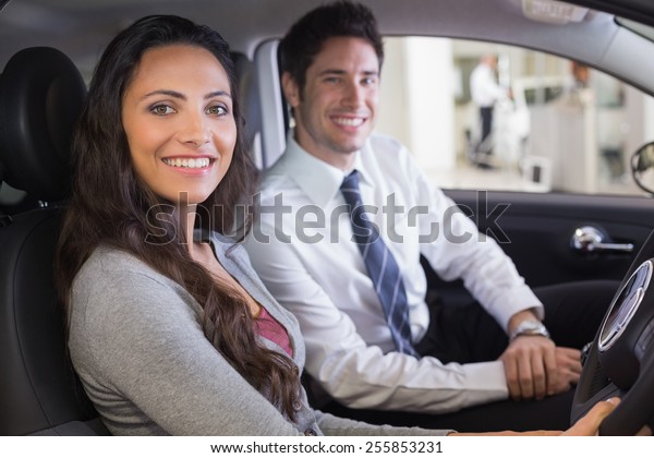 Female driver at the wheel sitting in her car\
with salesperson at new car\
showroom