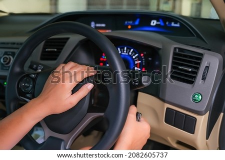 Female driver's hands on steering wheel and another on ignition key