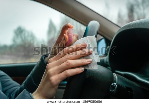 Female driver\'s hands wipe the\
steering wheel of the car with antiseptic and wipes\
close-up