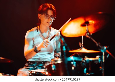 Female drummer energetically playing drum kit during live rock concert performance, illuminated by colorful stage lights, creating powerful and dynamic music - Powered by Shutterstock