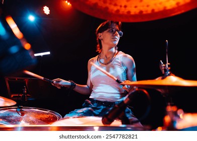 Female drummer energetically playing drums during a live concert, illuminated by vibrant red and blue stage lights, creating an electrifying atmosphere - Powered by Shutterstock