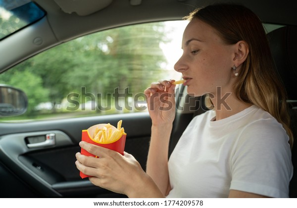 Female eating fries in the car. Hands\
holding a paper bag with fast food fried\
potatoes.