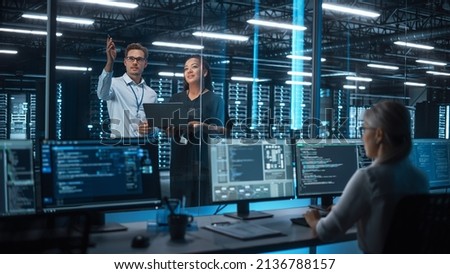 Female e-Business Entrepreneur and Male IT Specialist Discussing Something and Use Laptop in Big Data Center Server Room. Work on Web Services Cloud Computing SAAS Concept
