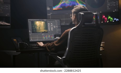 Female editor works in modern studio on computer using professional editing software. Woman edits video footage, makes color grading for movie post production. Big screen with RGB graphic on the wall. - Shutterstock ID 2288812425