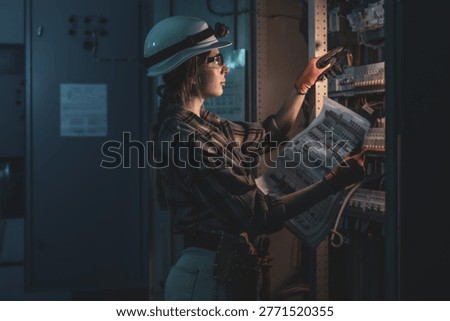Female electrical engineer checking power system diagram near switchboard. Professional inspection.