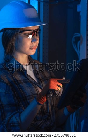 Female electrical engineer using tablet near industrial switchboard. Digital system control.