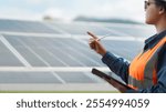 Female electrical engineer wearing hard hat inspecting solar farm panel equipment. Eco-friendly energy. Renewable clean energy technology concept.