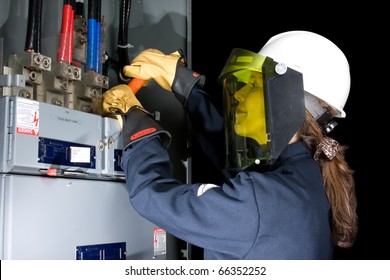 Female Electrician With Protective Clothing Performing Work In An Energized Panel With A Happy Smile. All Trade Marks Removed Or Modified