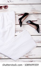 Female elegant clothes and accessories. Women white costume trousers, black lacquered heels and sunglasses, top view. Feminine trendy outfit.