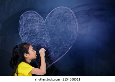 Female Elementary School Student Drawing A Heart Symbol On The Chalkboard In The Classroom At School