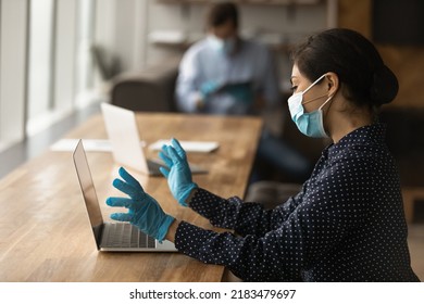 Female employee in facial mask and rubber gloves sit at desk in office work on computer during covid-19 pandemics. Woman worker in facemask talk on video call on laptop. Corona virus concept. - Powered by Shutterstock