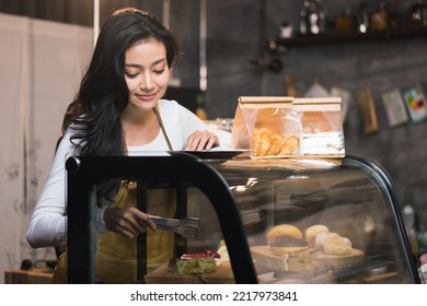 A female employee is happily picking up a bakery to serve it to customers in a cafe. - Powered by Shutterstock