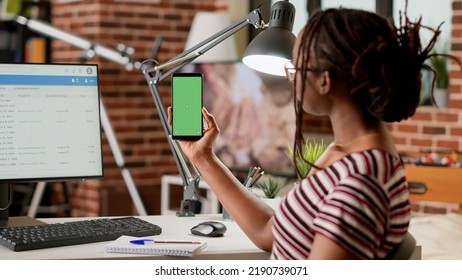 Female Employee Holding Smartphone With Greenscreen Display At Home, Working Remotely. Woman Looking At Mobile Phone With Isolated Chroma Key, Blank Copyspace Template And Mockup Background.