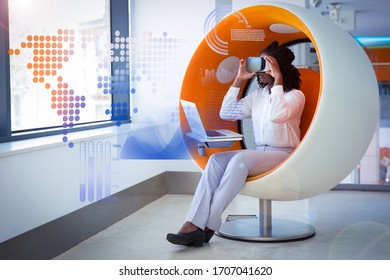 Empleada con gráficos estadísticos virtuales y portátiles. Mujer negra vestida de oficina y gafas de realidad virtual sentada en silla interactiva y sosteniendo auriculares. Concepto de experiencia VR