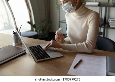 Female employee sit in office wear protective face mask disinfect computer with antibacterial liquid gel protect from coronavirus, woman sanitize laptop workplace with sanitizer from covid-19 pandemic - Powered by Shutterstock