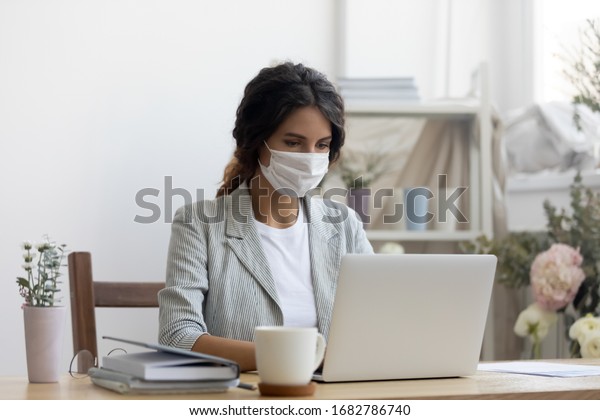 Female employee wear medical protective mask from\
covid-19 coronavirus pandemic work on laptop in office, woman in\
face cover from corona virus busy using computer at workplace,\
epidemic concept