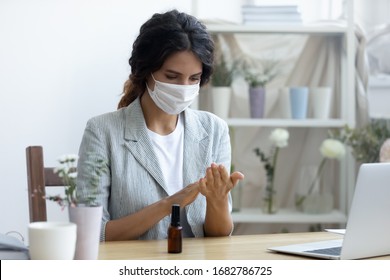 Female employee wear protective medical mask use hand sanitizer from covid-19 coronavirus pandemic, woman worker in face cover sanitize with liquid antibacterial gel in office, corona virus concept