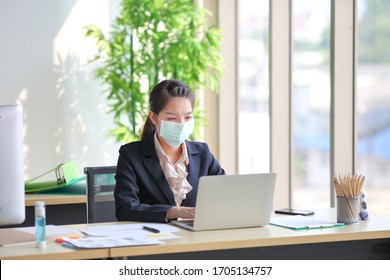 Female Employee Wearing Medical Facial Mask While Working Alone Because Of Social Distancing Policy In The Business Office Reopening During Coronavirus Or Covid-19 Outbreak Pandemic Situation