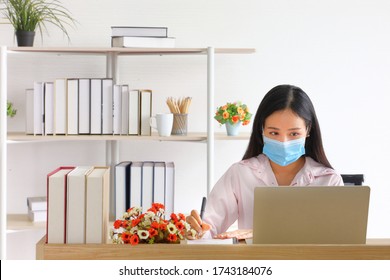 Female employee wearing medical facial mask working from home as social distancing policy in the business office during new normal change after coronavirus or post covid-19 with copy space - Powered by Shutterstock