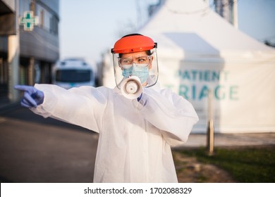 Female EMS ICU Paramedic In Personal Protective Equipment PPE Holding Megaphone Shouting Commands,standing In Front Of UK Hospital Exterior Patient Triage Tent,COVID-19 Pandemic Outbreak Crisis