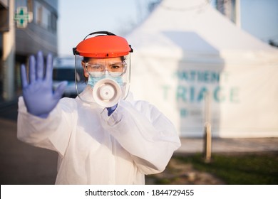 Female EMS ICU Paramedic In Personal Protective Equipment PPE Holding Megaphone Shouting Commands,standing In Front Of UK Hospital Exterior Patient Triage Tent,COVID-19 Pandemic Outbreak Crisis