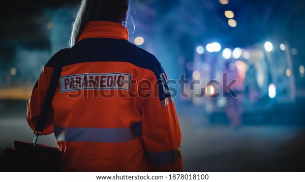 Female EMS Paramedic Proudly Standing With Her\
Back Turned to Camera in High Visibility Medical Orange Uniform\
with \