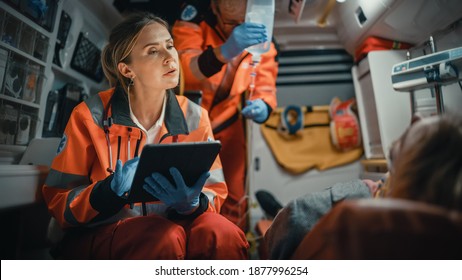Female EMS Professional Paramedic Using Tablet Computer to Fill a Questionnaire for the Injured Patient on the Way to Hospital. Emergency Care Assistant Comforting the Patient in an Ambulance.