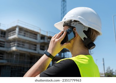 Female engineer at construction site of a building. Woman supervisor talking on the phone. Professional architect businesswoman wearing hard hat safety helmet and reflective clothing vest. - Powered by Shutterstock