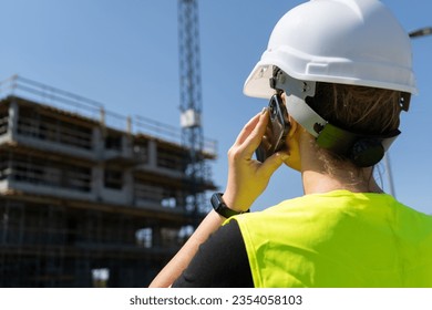 Female engineer at construction site of a building. Woman supervisor talking on the phone. Professional architect businesswoman wearing hard hat safety helmet and reflective clothing vest. - Powered by Shutterstock