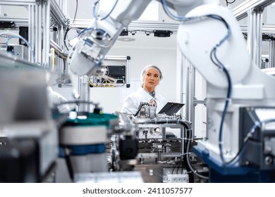 Female engineer controlling production process of modern robotic arm machine in automotive industry.