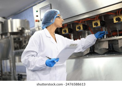 Female engineer in a drinking water factory in professional uniform using laptop working in beverage industrial. Female factory worker use notebook testing program in production line. - Powered by Shutterstock