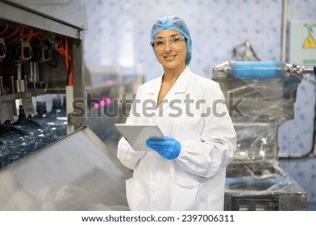 Female engineer in a drinking water factory in professional uniform using laptop working in beverage industrial. Female factory worker use notebook testing program in production line.