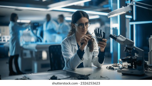 Female Engineer Fixing a High-Tech Bionic Hand Component. On Blurred Background Industrial Robotics Specialists in Lab Coats Working on a Mobile AI Robot in a Tech Factory Facility - Powered by Shutterstock