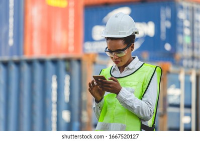 Female Engineer In The Hard Hat Uses Mobile Phone, Industrial Worker Using Mobile Smartphone In Industry Containers Cargo