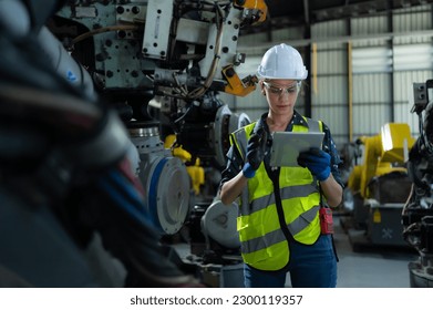 A female engineer installs a program on a robotics arm in a robot warehouse. And test the operation before sending the machine to the customer.